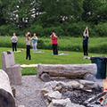 five women practicing yoga near campfire