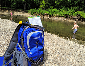 adventure backpack in foreground kids playing in creek in background