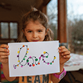 girl holding up a paper with the word "love" decorated using finger paint