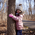 young girl in a pink winter coat hugging a tree trunk