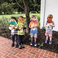 four children holding paper masks on brick sidewalk