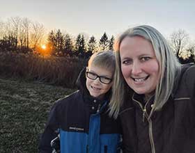 Woman and child in a field with the sun setting behind them.