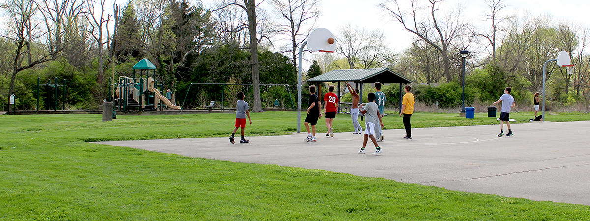 boys playing basketball at Concept Park, playground and shelter in background.