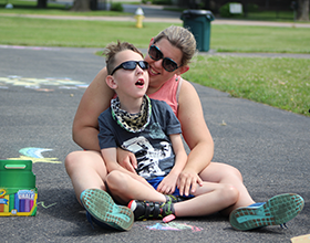 mother and son sitting on paved path creating chalk art