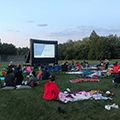 people watching a movie in the park on a big screen