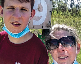 man and woman in front of bluebird box, face mask on chins