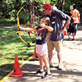 young girl shooting a bow and arrow with an instructor's guidance