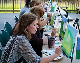 women sitting outside on a deck painting nature scenes