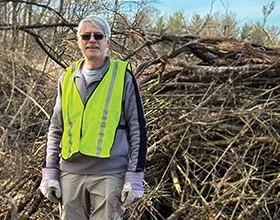 Man in a yellow safety vest standing in front of a pile of honeysuckle