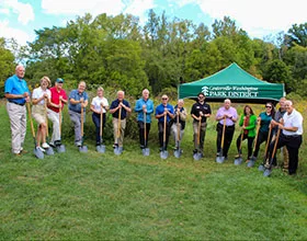 A group of people in a field with shovels. A Centerville-Washington Park District tent appears behind them.