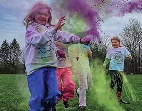 four children getting color powder thrown on them during a fun run