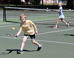 two children with tennis racquets and tennis balls on a tennis court