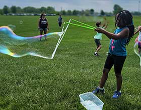 young girls with a big bubble, people in a field in the background