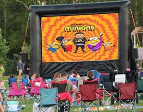 Inflatable movie screen with people sitting in front of it in lawn chairs