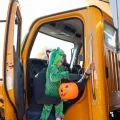 Girl dressed as a green dragon holding a pumpkin bucket coming out of a dump truck cab