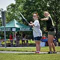 Two people with an archery bow. Green Centerville-Washington Park District tent in the background.