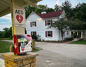 AED cabinet on a park shelter pole. House in the background.