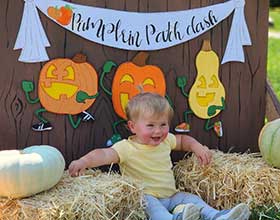 Toddler sitting between two bales of hay. A sign above the toddler's head says Pumpkin Patch Dash.