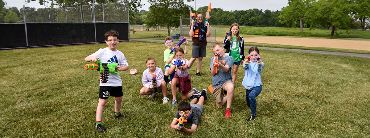 A group of children outside. They are holding Nerf guns and looking toward the camera.