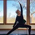a woman sitting on a chair doing a yoga pose in front of a large window