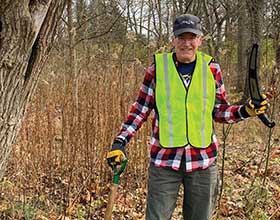 a man in a high visability vest standing in a field with his hand on a shovel