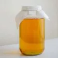 a jar of golden colored kombucha covered with cloth, sitting on a table