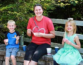 An adult and two children sitting on a stone wall eating ice cream